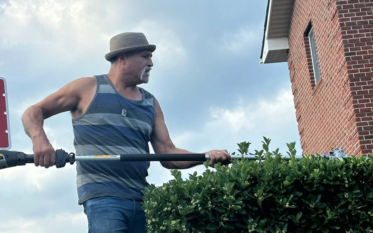 Greenscape crew member trimming a tall hedge with a pole trimmer
