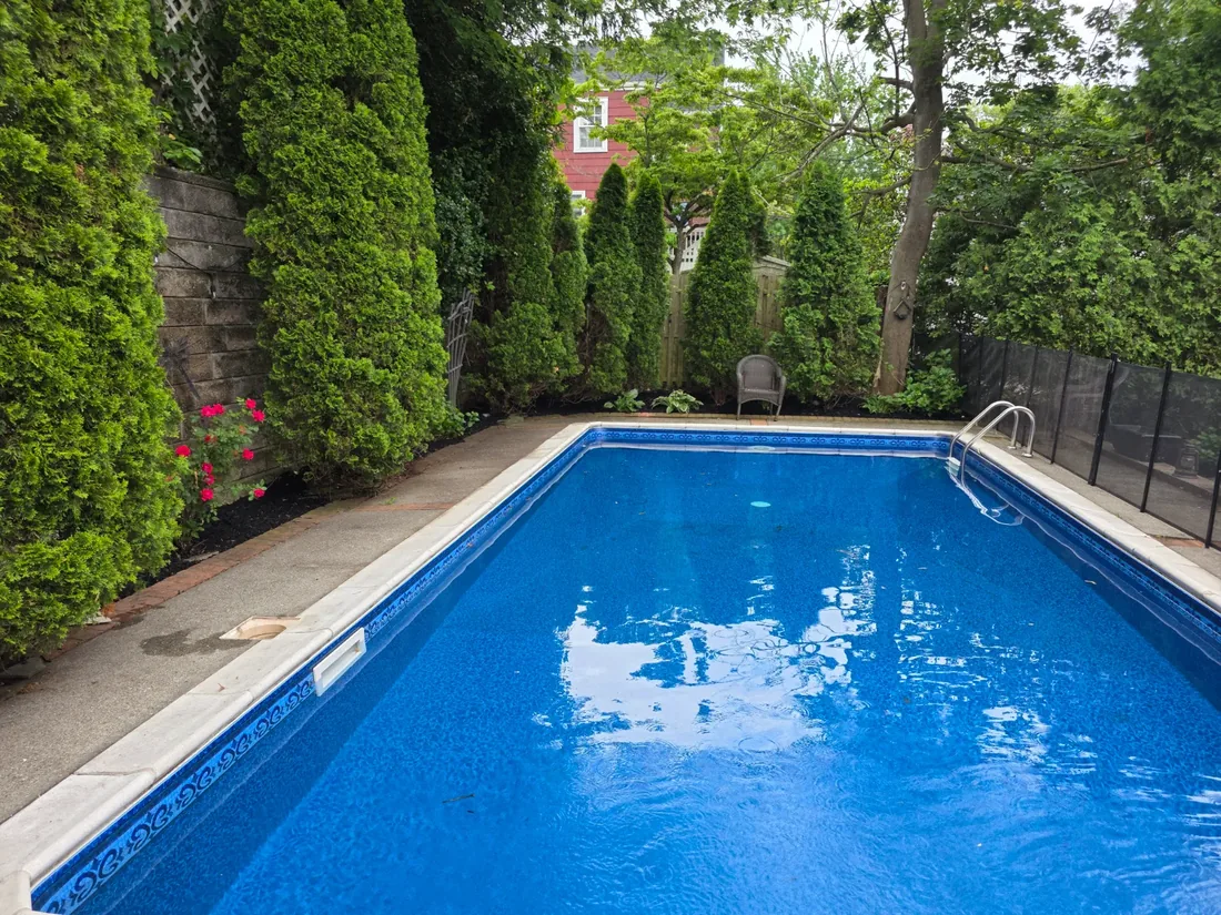 Backyard pool bordered by tall trimmed hedges and maintained beds