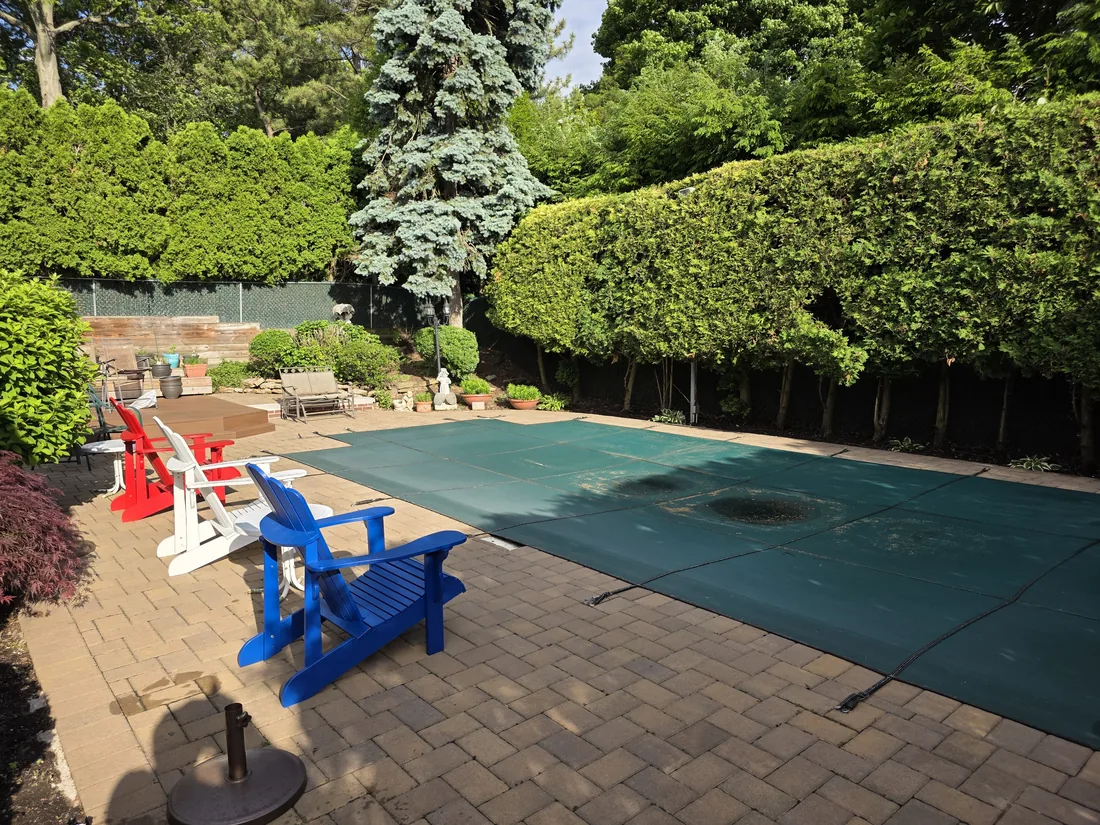Covered pool and paver patio framed by a trimmed privacy hedge