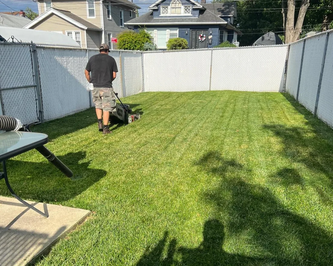 Crew member mowing a fenced backyard lawn