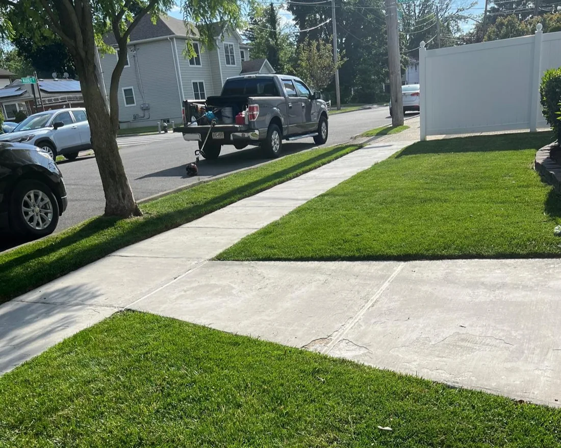 Front lawn cut and edged cleanly along the sidewalk, work truck at the curb